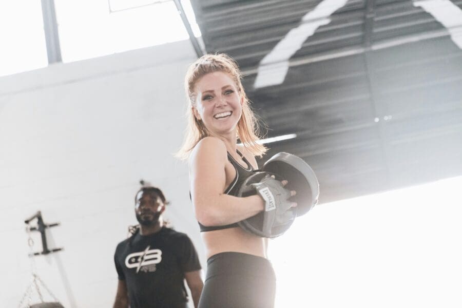 A boxing coach and a client smile at the camera whilst working out 